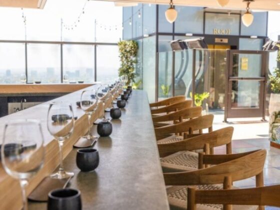 Rooftop dining bar with a long counter set for service, wine glasses lined up and sunlight streaming in.