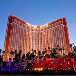 Treasure Island hotel and casino in Las Vegas at dusk, curved white towers with palm trees and bright exterior lighting.