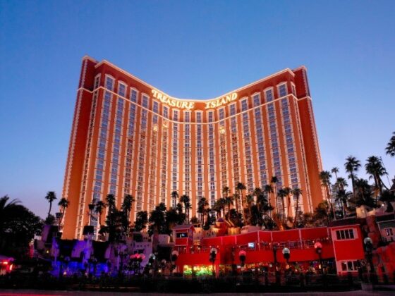 Treasure Island hotel and casino in Las Vegas at dusk, curved white towers with palm trees and bright exterior lighting.