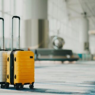 Two rolling suitcases, white and yellow, with extended handles, standing in a modern airport terminal.