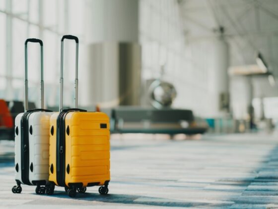 Two rolling suitcases, white and yellow, with extended handles, standing in a modern airport terminal.