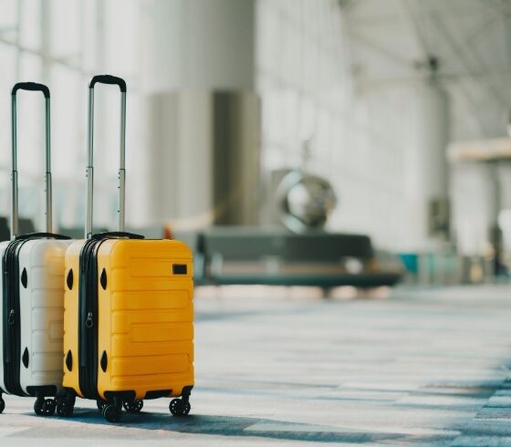 Two rolling suitcases, white and yellow, with extended handles, standing in a modern airport terminal.