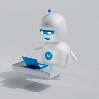 White robot with blue visor and AI badge working at a laptop on a desk