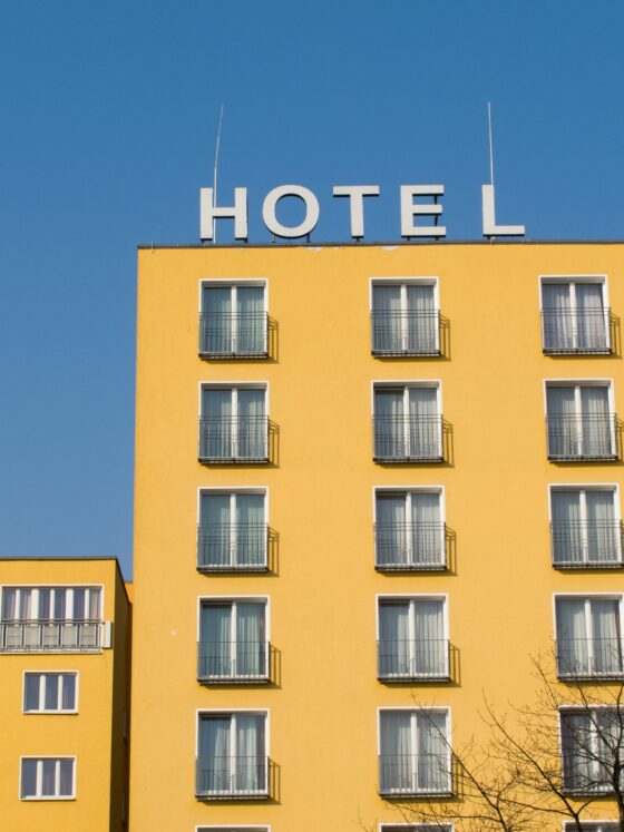 Yellow hotel building with many windows and small balconies under a clear blue sky; HOTEL sign on the roof.
