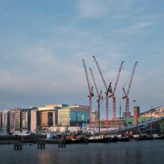 Cluster of red construction cranes rising over a modern waterfront cityscape at dusk.
