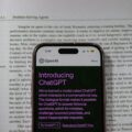 Smartphone screen showing the OpenAI ChatGPT app with a purple 'Introducing ChatGPT' headline over a printed article background.