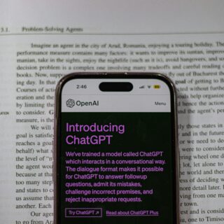 Smartphone screen showing the OpenAI ChatGPT app with a purple 'Introducing ChatGPT' headline over a printed article background.