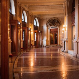 Luxurious historic hall with tall arches, marble columns, and glass display cases along a warm, ornate corridor.
