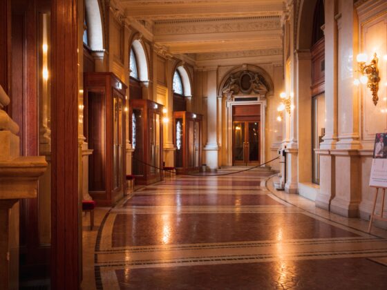 Luxurious historic hall with tall arches, marble columns, and glass display cases along a warm, ornate corridor.