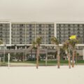 Beachfront Embassy Suites hotel seen from the sandy foreground, with palm trees and a row of balconies.