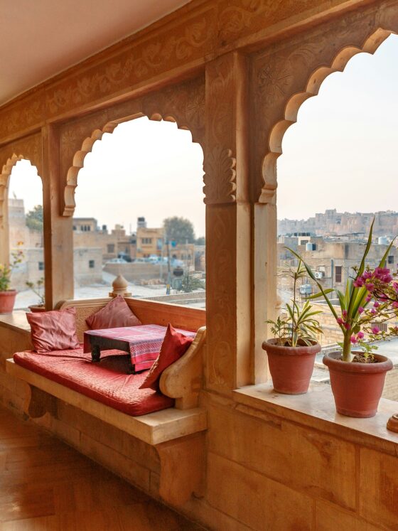 Terrace with carved wooden arches, red cushions, and potted plants overlooking a cityscape at dusk.