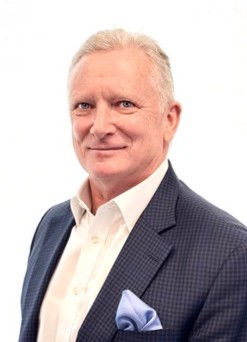 Portrait of a smiling older man in a navy check blazer and white shirt, with a light blue pocket square.