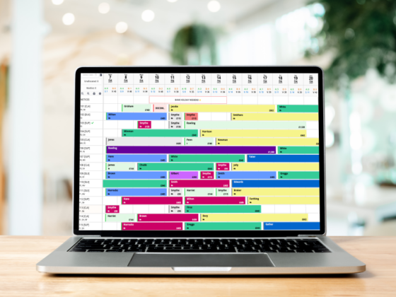 Open laptop on a wooden table displaying a colorful weekly schedule calendar on screen in a bright office setting.