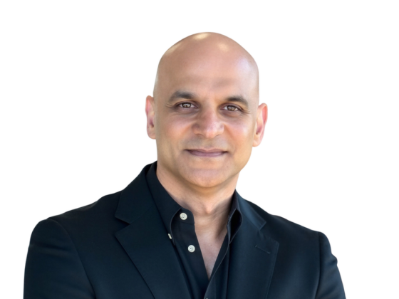 Professional headshot of a smiling, bald man in a black blazer against a white background.