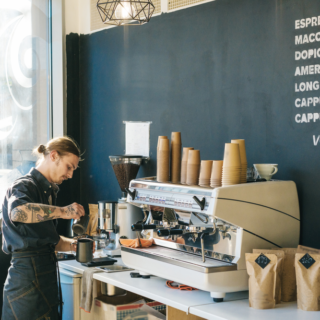 Barista with tattoos operating a commercial espresso machine behind a counter.