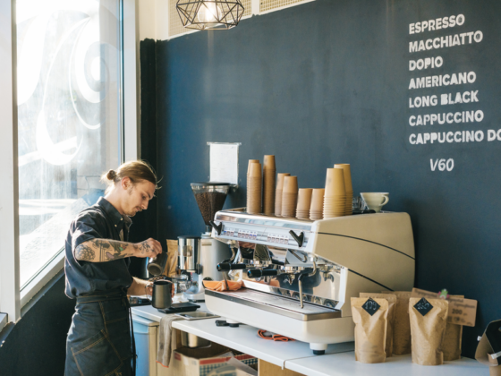 Barista with tattoos operating a commercial espresso machine behind a counter.