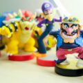 Close-up of a colorful toy figure with a helmet and mustache, surrounded by other blurred toy characters on a table.