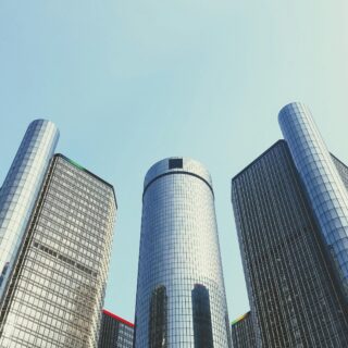 Tall glass skyscrapers viewed from street level, reaching up toward a clear blue sky.
