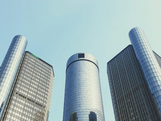 Tall glass skyscrapers viewed from street level, reaching up toward a clear blue sky.