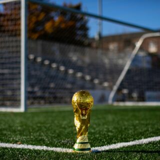 Golden World Cup trophy placed on a grassy soccer field with a blurred goal in the background.