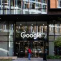 Exterior view of a Google office building with a large white 'Google' logo on glass facade and pedestrians nearby.