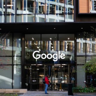 Exterior view of a Google office building with a large white 'Google' logo on glass facade and pedestrians nearby.