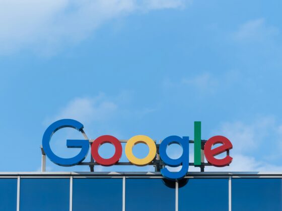 Google wordmark with multicolored letters mounted on a building under a blue sky.