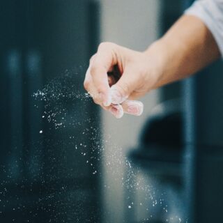 Close-up of a hand sprinkling flour, creating a powdery dust in the air.