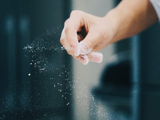Close-up of a hand sprinkling flour, creating a powdery dust in the air.