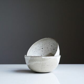 Stack of speckled ceramic bowls stacked on a white surface against a dark gray background.