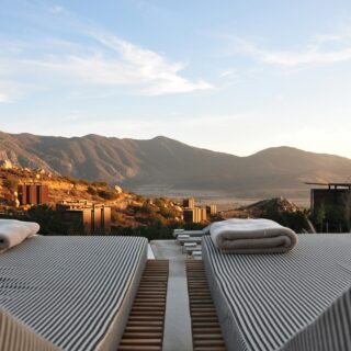 Row of striped lounge chairs with towels at a resort pool, desert mountains in the background under a clear sky.