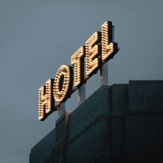 Rooftop sign outlined with warm light bulbs against a dusky blue sky; part of a building façade is visible below.