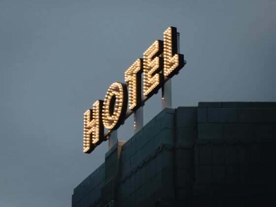 Rooftop sign outlined with warm light bulbs against a dusky blue sky; part of a building façade is visible below.