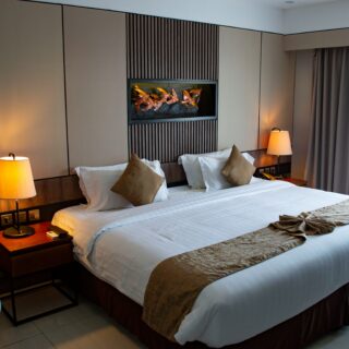 Hotel room with two beds, white linens, beige headboard wall, and warm bedside lamps on wooden nightstands.