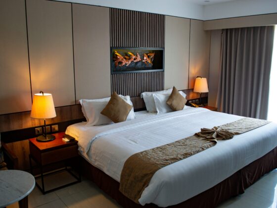 Hotel room with two beds, white linens, beige headboard wall, and warm bedside lamps on wooden nightstands.