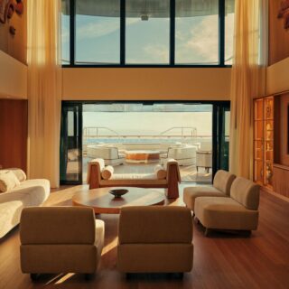 Luxurious yacht lounge with beige sofas and wooden coffee tables, glass doors open to an outdoor deck and sea view.