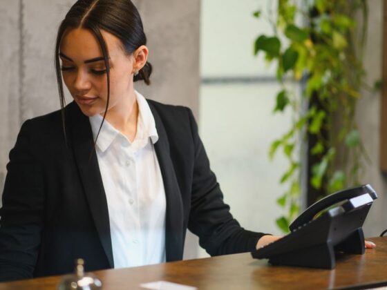 Professional woman in a black blazer at a reception desk, using a desk phone.