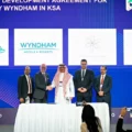 Five men in business attire stand behind a signing table during a ceremony, with a blue backdrop displaying logos (Ministry of Tourism, Wyndham, Super 8).
