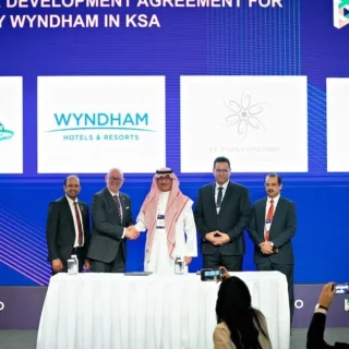 Five men in business attire stand behind a signing table during a ceremony, with a blue backdrop displaying logos (Ministry of Tourism, Wyndham, Super 8).
