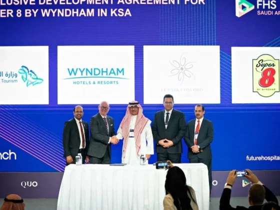 Five men in business attire stand behind a signing table during a ceremony, with a blue backdrop displaying logos (Ministry of Tourism, Wyndham, Super 8).