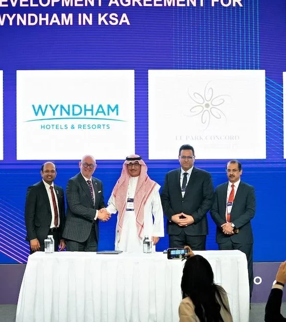 Five men in business attire stand behind a signing table during a ceremony, with a blue backdrop displaying logos (Ministry of Tourism, Wyndham, Super 8).