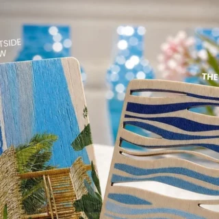 Two decorative wooden panels — left with a tropical beach scene, right with blue wave-cut patterns — blurred blue bottles and flowers in the background.