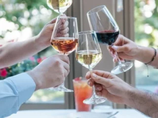 Group of people toasting with raised wine glasses at a table by a window.