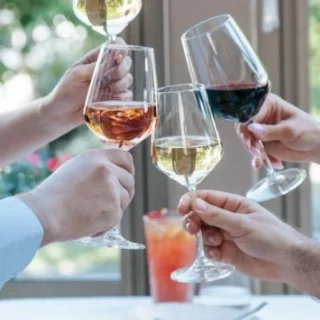 Group of people toasting with raised wine glasses at a table by a window.