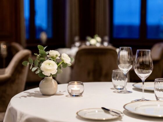 Table set for two in a fine dining room with a small floral centerpiece and candle on the table.
