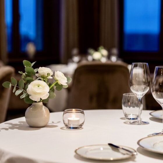 Table set for two in a fine dining room with a small floral centerpiece and candle on the table.