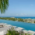 Infinity pool overlooking a tropical coastline with white loungers and palm fronds overhead.
