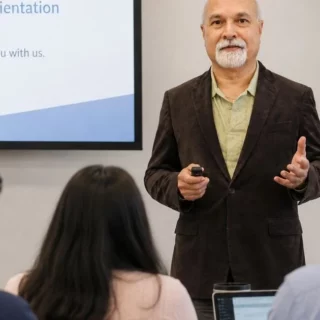 Man presenting to a group during onboarding; slide reads 'Onboarding & Orientation' with a welcoming message.