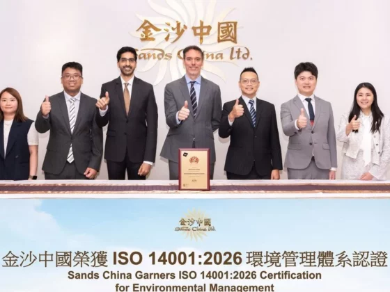 Group of eight professionals posing behind a table, thumbs up, celebrating Sands China Ltd. ISO 14001:2026 certification achievement.