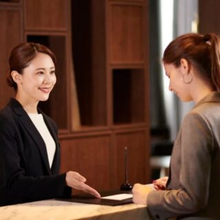 Receptionist in a blazer greets a guest at a marble front desk in a lobby; UNIFOCUS logo visible on the top-left corner.